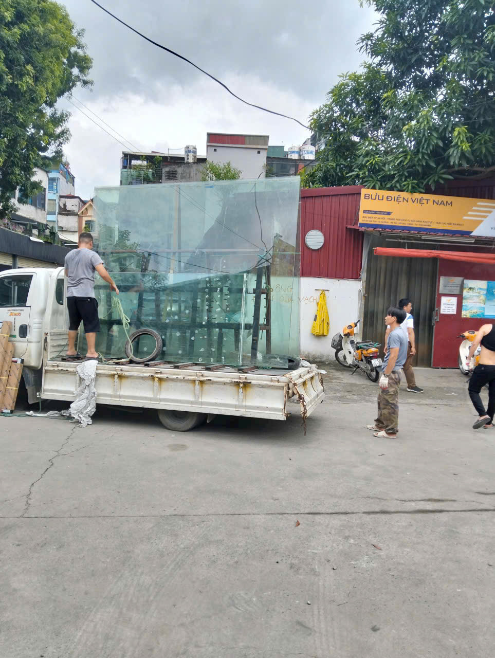 Các tấm kính lớn trong suốt được xếp trên xe tải để vận chuyển cùng công nhân đang bốc dỡ񎟿